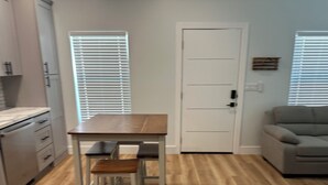 A kitchen with a wooden table and two bar stools, a gray sofa, and a white door.