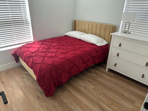 A bedroom with a bed, a dresser, and a window with blinds.