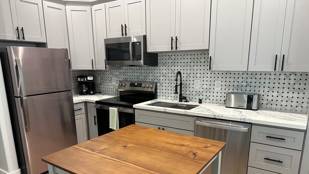 A modern kitchen with stainless steel appliances, white cabinets, and a wooden table.