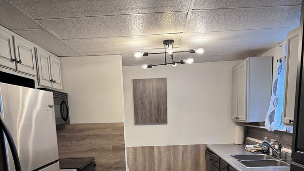 A modern kitchen with a stainless steel refrigerator, black cabinets, a wooden floor, and a light fixture with multiple bulbs.