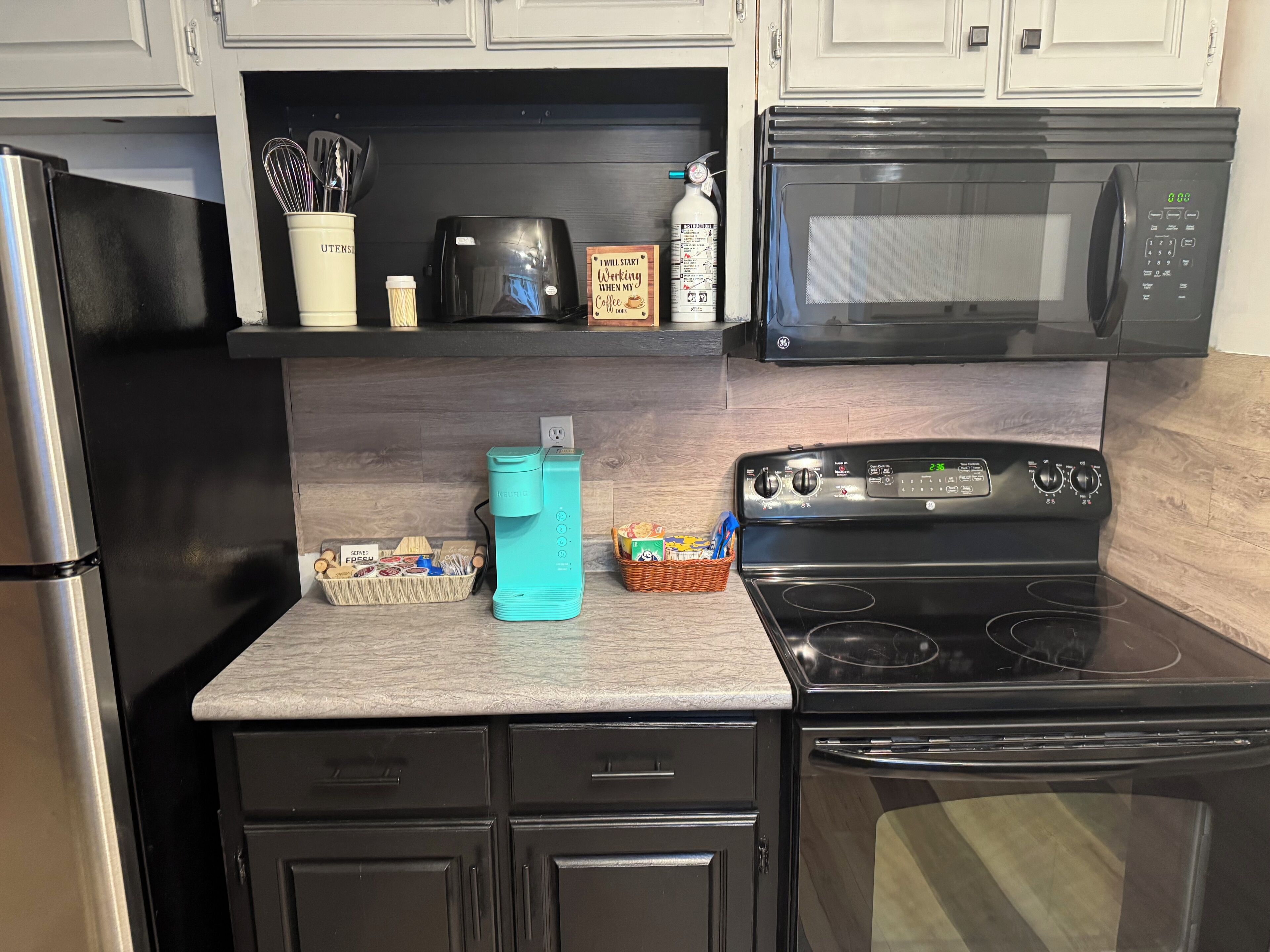 A kitchen with a black refrigerator, a microwave, a stove, and a coffee maker.