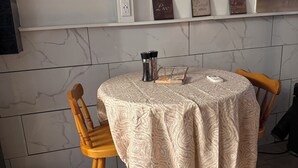 A dining area with a round table covered by a patterned tablecloth, two wooden chairs, and a wall-mounted air conditioner.