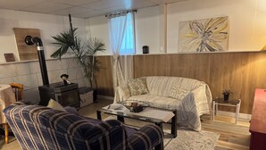 A living room with a sofa, armchair, and a coffee table. There is a fireplace, a plant, and a painting on the wall.