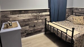 A bedroom with a wooden headboard, a bed with patterned bedding, a nightstand with a lamp, and a blue curtain.