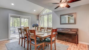 Un coin repas avec une table et des chaises en bois, un piano et un ventilateur de plafond.