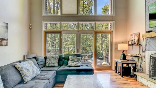 Un salon moderne avec un canapé d’angle, une cheminée et de grandes fenêtres donnant sur la forêt.