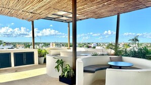 An outdoor patio with a curved seating area, a round table, and potted plants. - Modern Studio, Pool, WiFi, min Sea and 5th Ave. (Playa del Carmen)