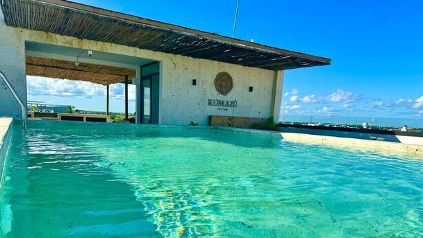 A clear swimming pool with a building labeled "KUMARU SUITES" in the background. - Modern Studio, Pool, WiFi, min Sea and 5th Ave. (Playa del Carmen)