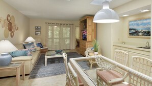 A living room with a sofa, coffee table, and chairs, a dining area with a table and chairs, and a kitchen with a sink and cabinets.