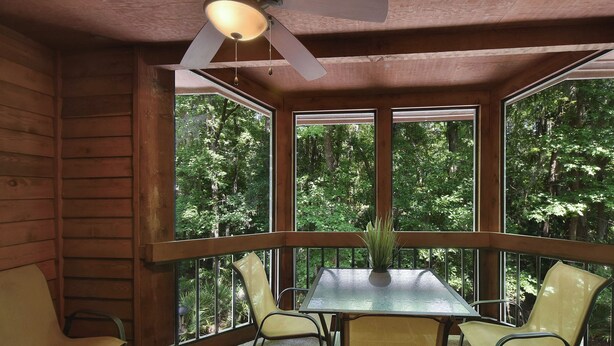 A wooden cabin with a dining table and chairs, large windows, and a ceiling fan.