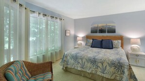 A bedroom with a bed, a nightstand, a lamp, a chair, and a window with curtains.