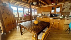 A wooden dining table with a bowl, a wooden bench, a wooden kitchen with a window, and a wooden ceiling.