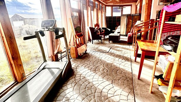 A spacious room with a treadmill, wooden furniture, and large windows offering a view of the outdoors.