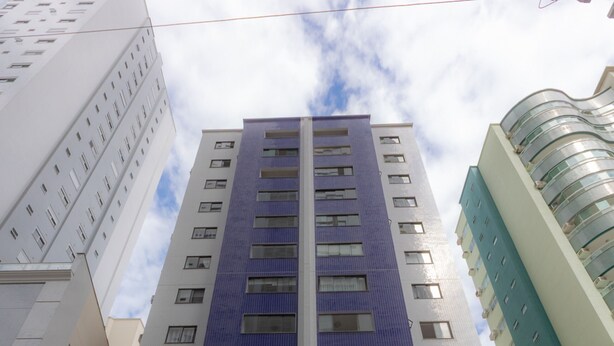 Un edificio moderno con llamativa fachada azul y blanca, varios pisos y una entrada a nivel de calle con puerta de vidrio.