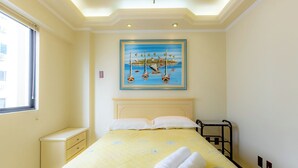 Habitación de hotel con cama, un cuadro de barcos en el agua, ventana y mesita de noche.