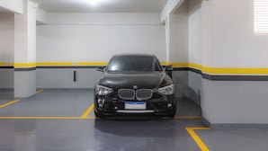 Un coche negro estacionado en un garaje con paredes blancas y líneas amarillas.