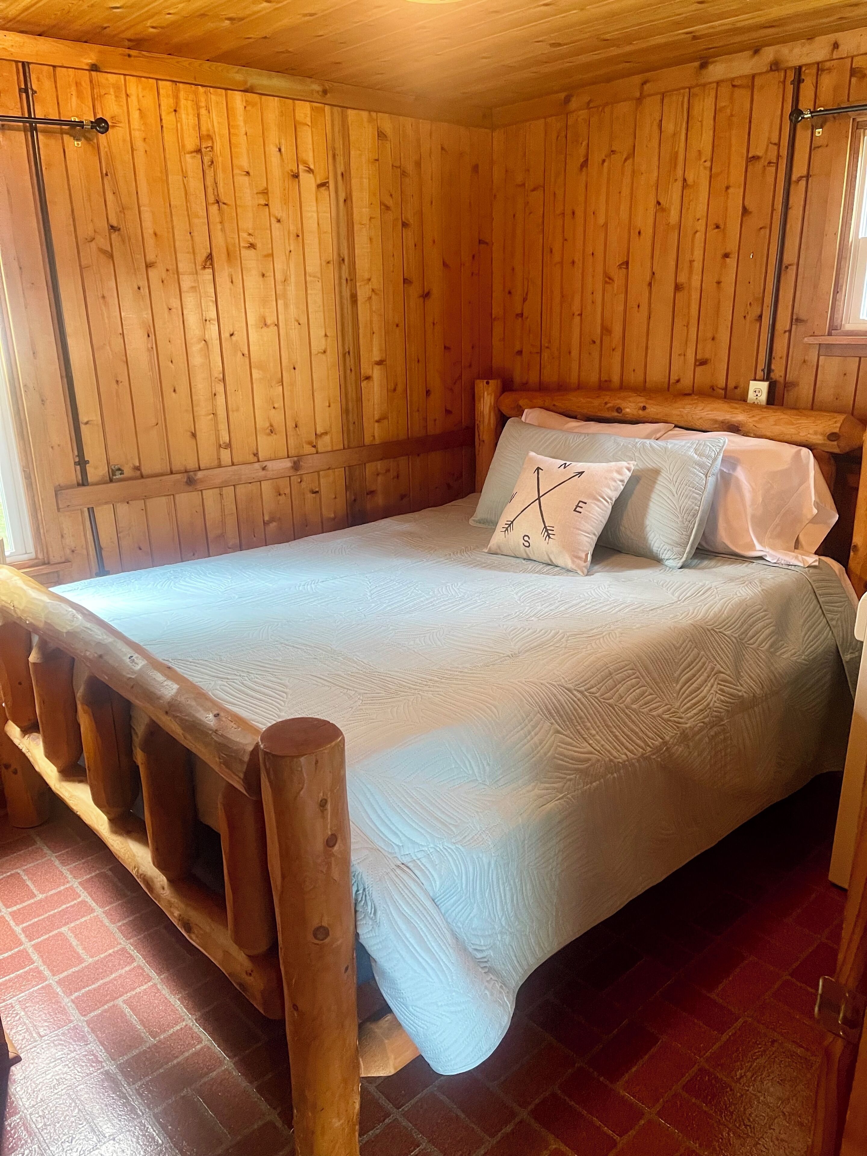 A wooden-paneled room with a bed, a brick floor, and a wooden bench.