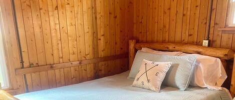 A wooden-paneled room with a bed, a brick floor, and a wooden bench.