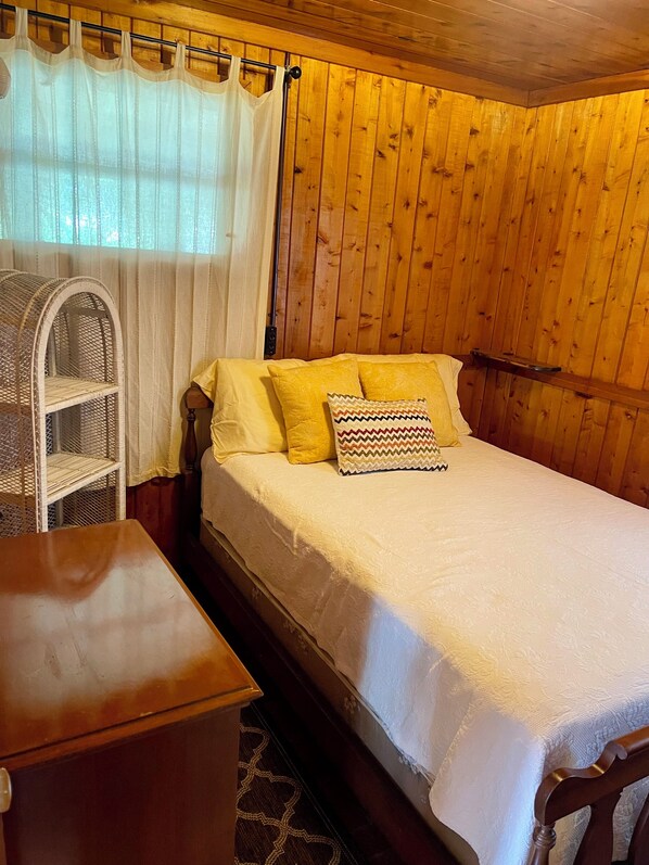 Ein Zimmer mit Holzwänden, einem Bett, einem Korbsessel und einem kleinen Tisch.