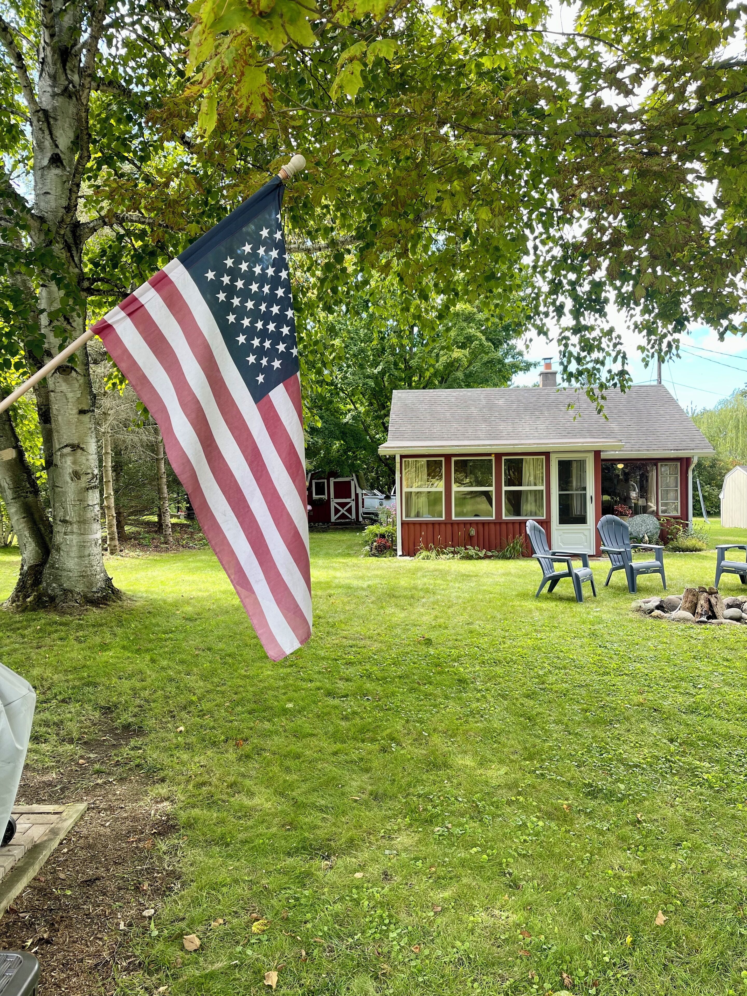 A house with a red exterior and white trim, a small porch with blue chairs, and an American flag in front.