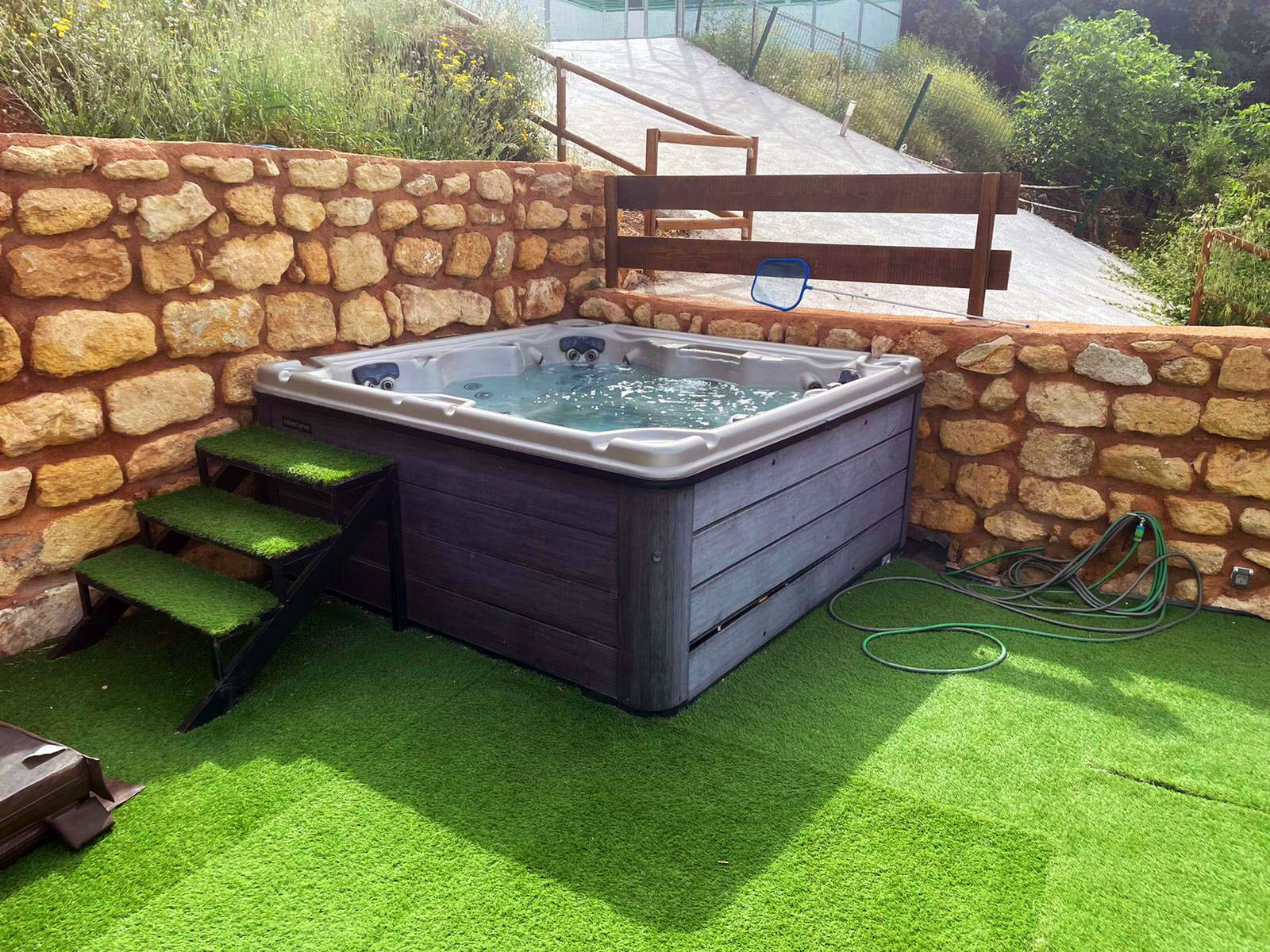 Un bain à remous installé dans un espace extérieur entouré de murs en pierre, accessible par des marches.