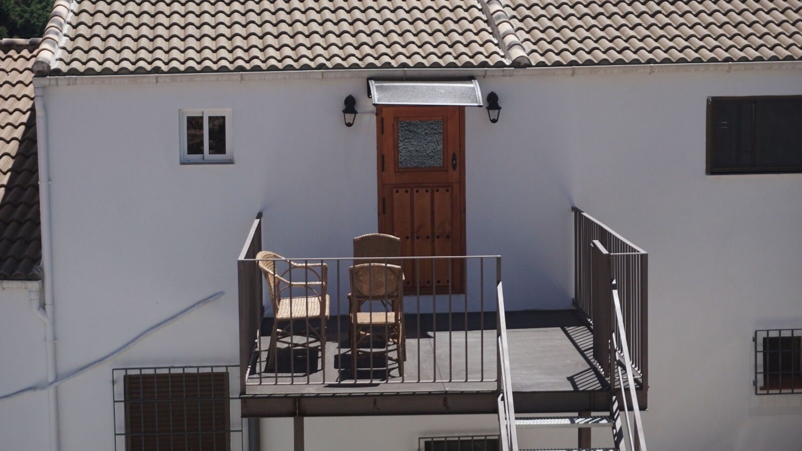 Een balkon met twee rieten stoelen en een houten deur.