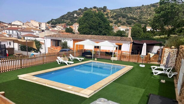 A swimming pool with a hot tub in the foreground, surrounded by a wooden fence and a grassy area. - Rural house torre chica located in frailes jaen in the middle of nature (frailes)