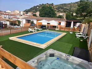 A swimming pool with a hot tub in the foreground, surrounded by a wooden fence and a grassy area. - Rural house torre chica located in frailes jaen in the middle of nature (frailes)
