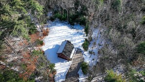Une cabane entourée d’une forêt, et le sol est couvert de neige.