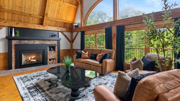 Ein geräumiges Wohnzimmer mit Kamin, Ledersofas, einem Couchtisch und großen Fenstern mit Blick ins Freie.
