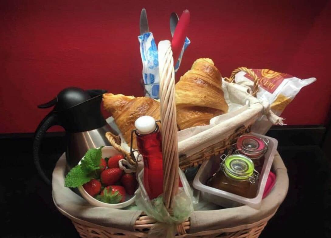 Un panier contenant des croissants, des fraises, une bouteille rouge et un thermos.