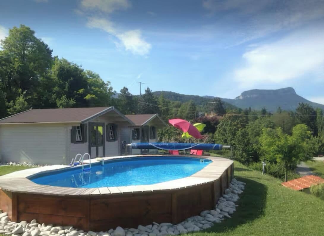 Un patio trasero con piscina, una terraza de madera y una montaña al fondo.