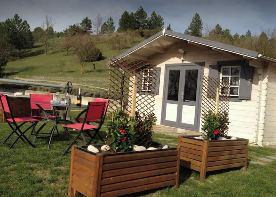 A small cabin with a wooden deck, red chairs, and planters with flowers.