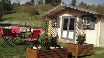 A small cabin with a wooden deck, red chairs, and planters with flowers.