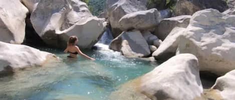 Une femme dans un environnement naturel, avec de l’eau claire et de gros rochers.