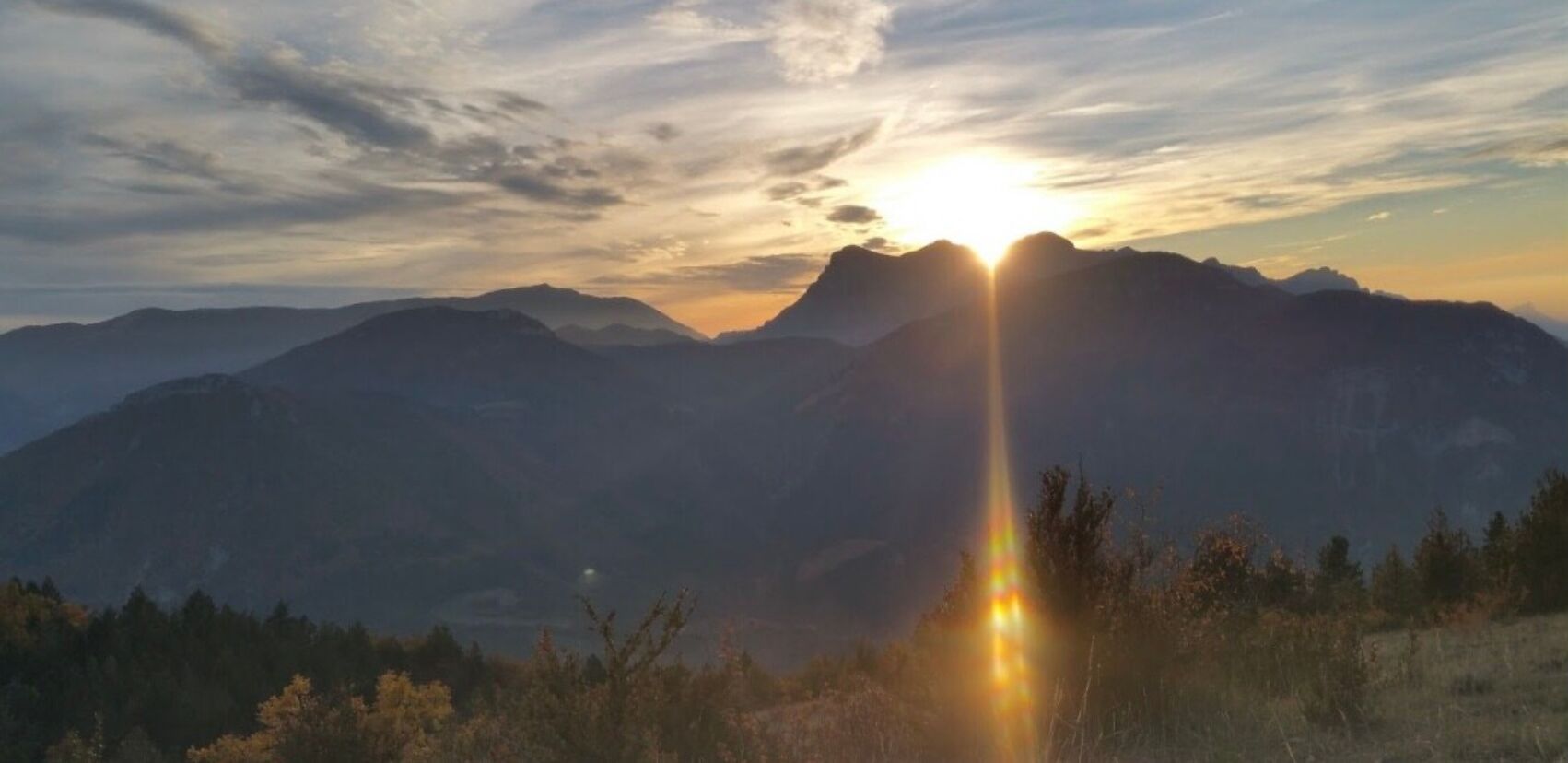 A mountain landscape with a sun setting behind the peaks.