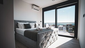Une chambre moderne avec un grand lit, une vue sur la ville grâce à une porte-fenêtre coulissante et un climatiseur fixé au mur.