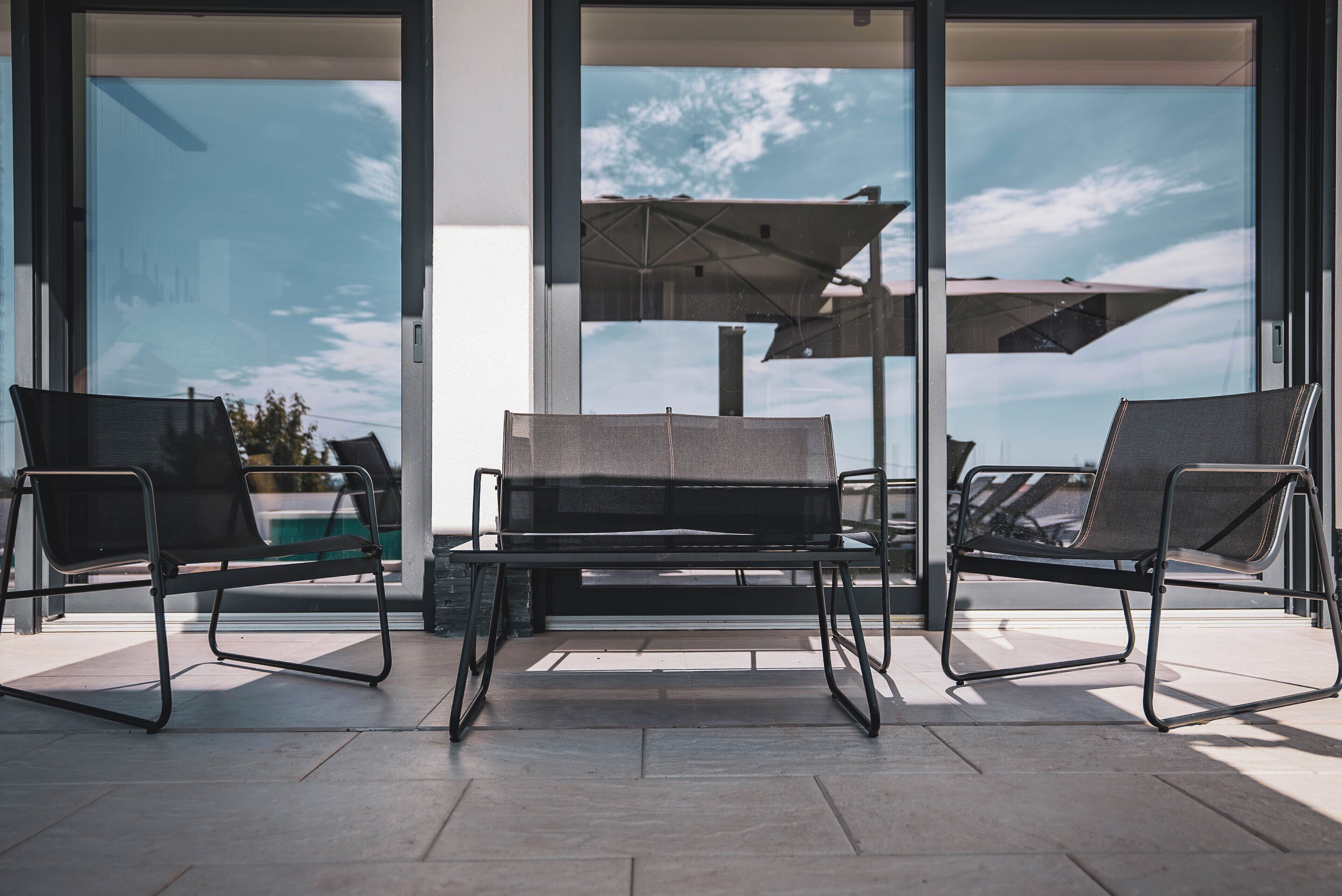 A modern outdoor seating area with a table and chairs, large windows, and a view of the sky.
