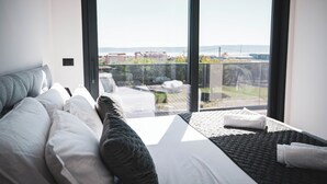 Ein modernes Hotelzimmer mit einem großen Bett, Blick auf die Stadt durch eine Schiebetür und einem Balkon mit Stadtpanorama.