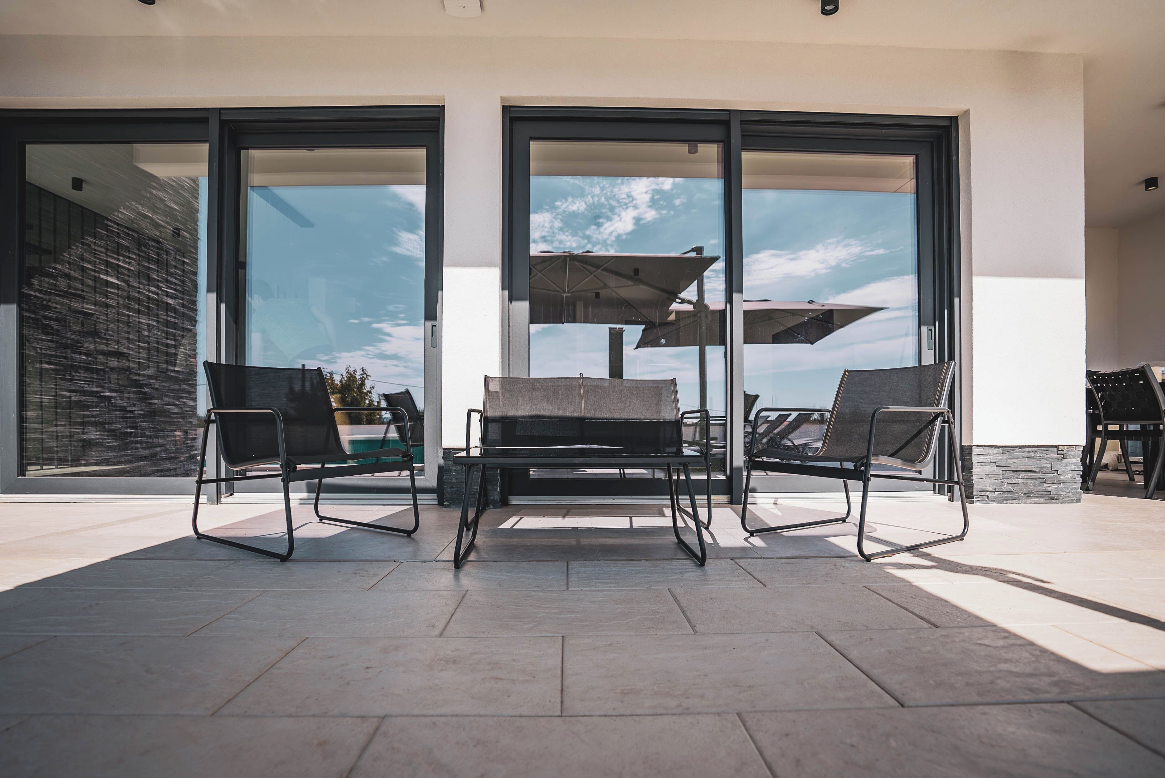 An outdoor patio with a modern seating arrangement, large sliding glass doors, and a view of the sky.