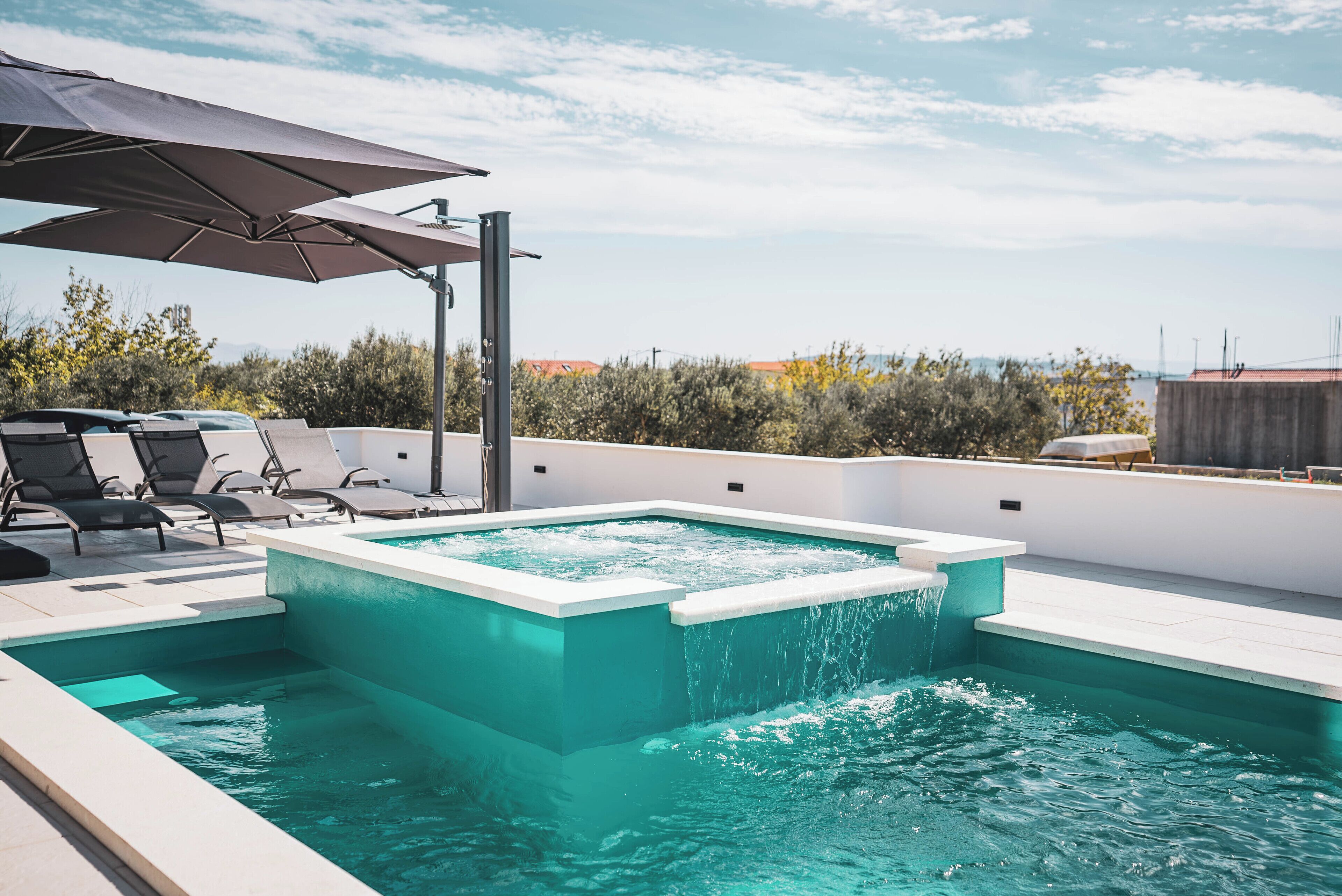 A rooftop pool with clear water, surrounded by lounge chairs and umbrellas, overlooking a cityscape.
