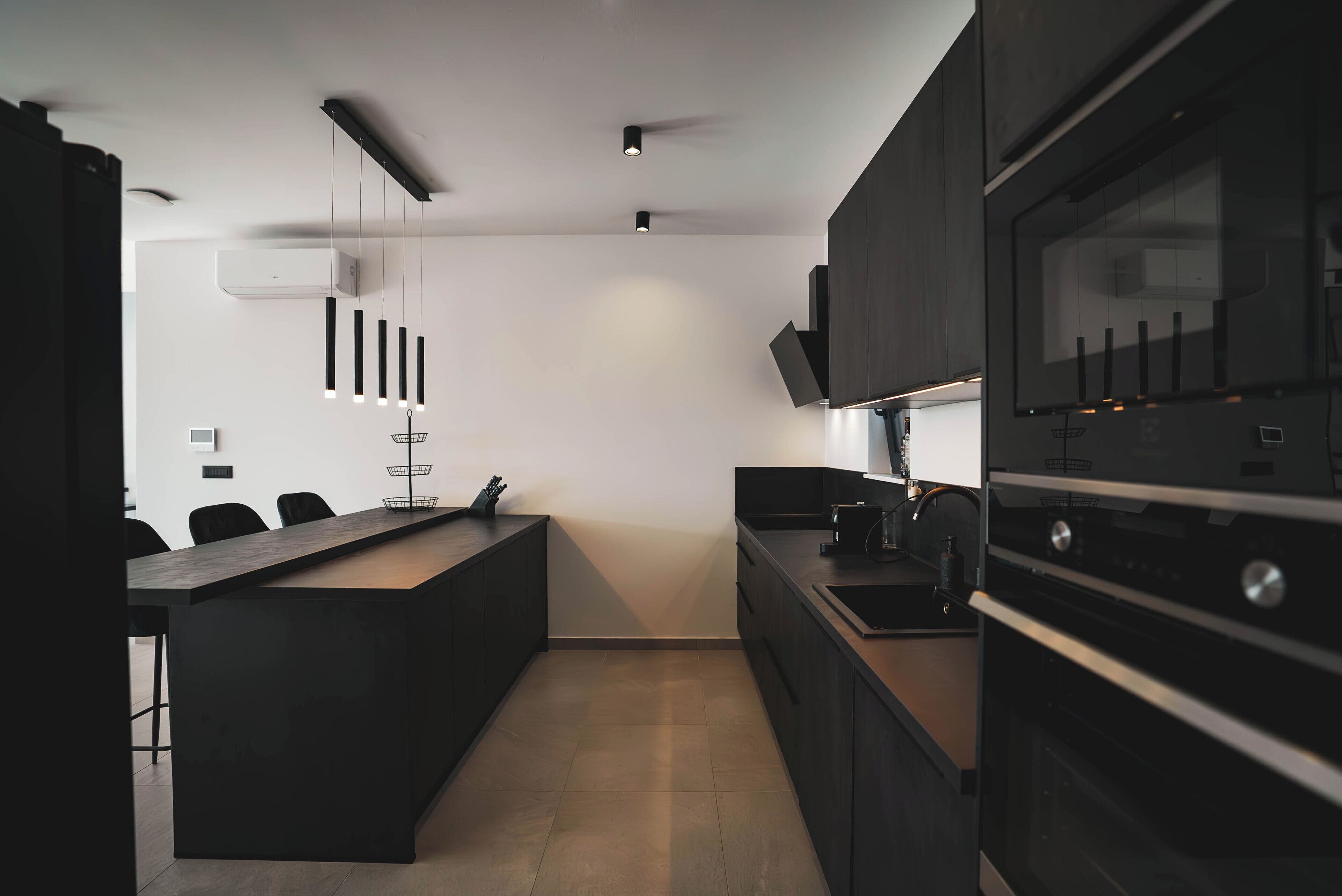 A modern kitchen with a central island, black cabinetry, and built-in appliances.