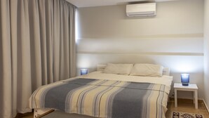 A bedroom with a bed, curtains, an air conditioner, and bedside lamps.