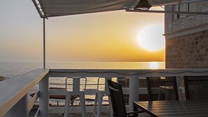 A terrace with a view of the sea at sunset, featuring a table and chairs.