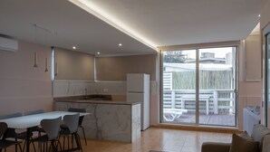 A modern kitchen with a marble island, dining area with chairs, and a large sliding glass door leading to an outdoor patio.