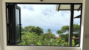 A modern room with a large window, a wooden bench with cushions, and a glass table. - Costa Rica dream: ocean view, infinity pool, surrounded by nature (Puntarenas Province)