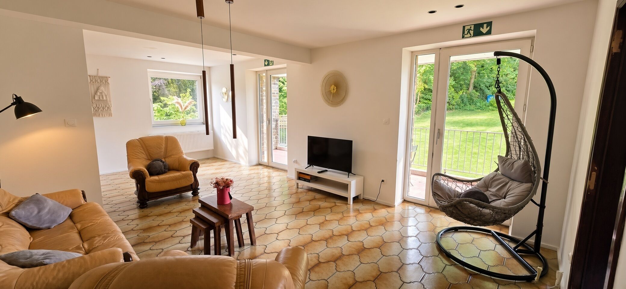 Een ruime woonkamer met een bank, een fauteuil, een televisie en een hangstoel.