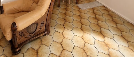 A room with a dining table, chairs, a sofa, and a patterned floor.