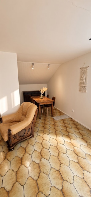 A room with a dining table, chairs, a sofa, and a patterned floor. - Chez Parrain (Sprimont)