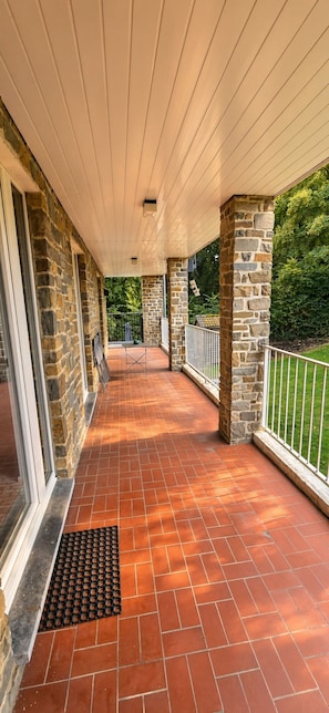 A covered outdoor area with stone pillars, a tiled floor, and a metal railing. - Chez Parrain (Sprimont)